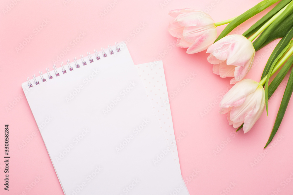 White notebook and spring flower pink tulips on the pink background. Theme of love, mother's day, women's day flat lay