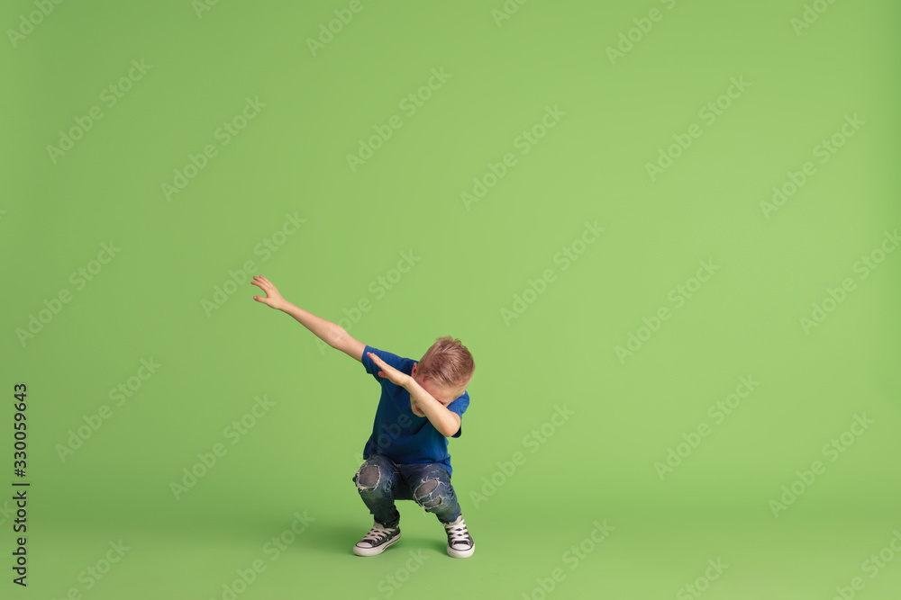 Dabbing. Happy boy playing and having fun on green studio background. Caucasian kid in bright cloth looks playful, laughting, smiling. Concept of education, childhood, emotions, facial expression. Dabbing. Happy boy playing and having fun on green studio background. Caucasian kid in bright cloth looks playful, laughting, smiling. Concept of education, childhood, emotions, facial expression.