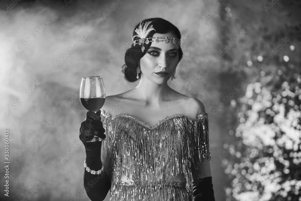 Fototapeta Czarno-biały portret  stylowej kobiety retro w połyskującej srebrnej sukience z lampką wina w ręku. 