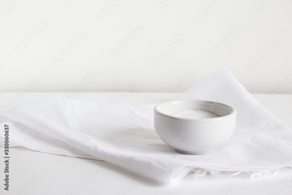 A salt shaker filled with white salt lies on a light towel on a gray background. A salt shaker filled with white salt lies on a light towel on a gray background.