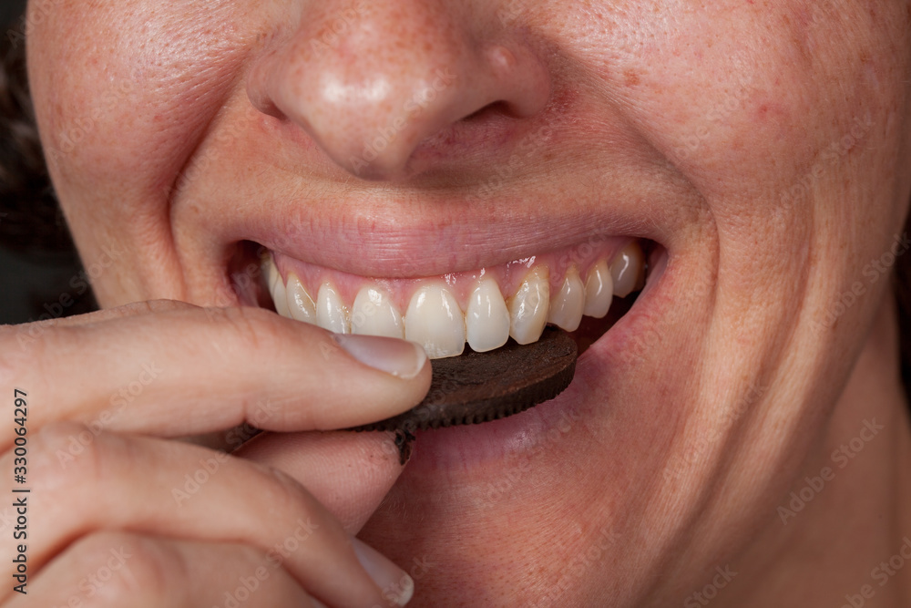 Close up of older woman eating a chocolate cream filled cookie.