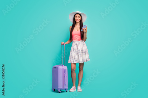 Full size photo positive girl tourist use cellphone book taxi service hold purple suitcase enjoy travel weekend wear white plaid checkered skirt pink singlet isolated pastel teal color background