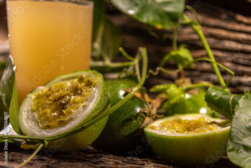 Glass of passion fruit juice among fresh broken fruits on a woody background