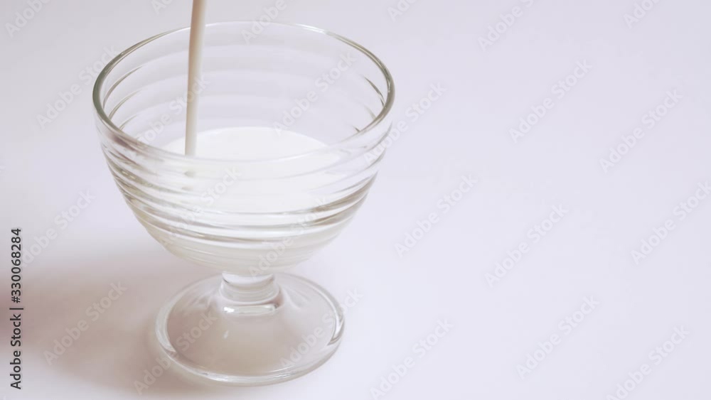 Organic milkshake in a glass cup. A person pours kefir into transparent container in isolation Organic milkshake in a glass cup. A person pours kefir into transparent container in isolation