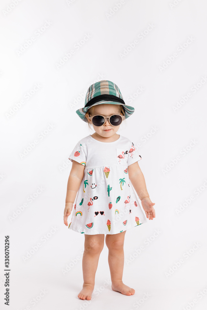 Portrait of a little cute girl wearing summer dress, blue checkered hat and fashion sunglasses isolated on white background. Concept of travel and summertime. Portrait of a little cute girl wearing summer dress, blue checkered hat and fashion sunglasses isolated on white background. Concept of travel and summertime.