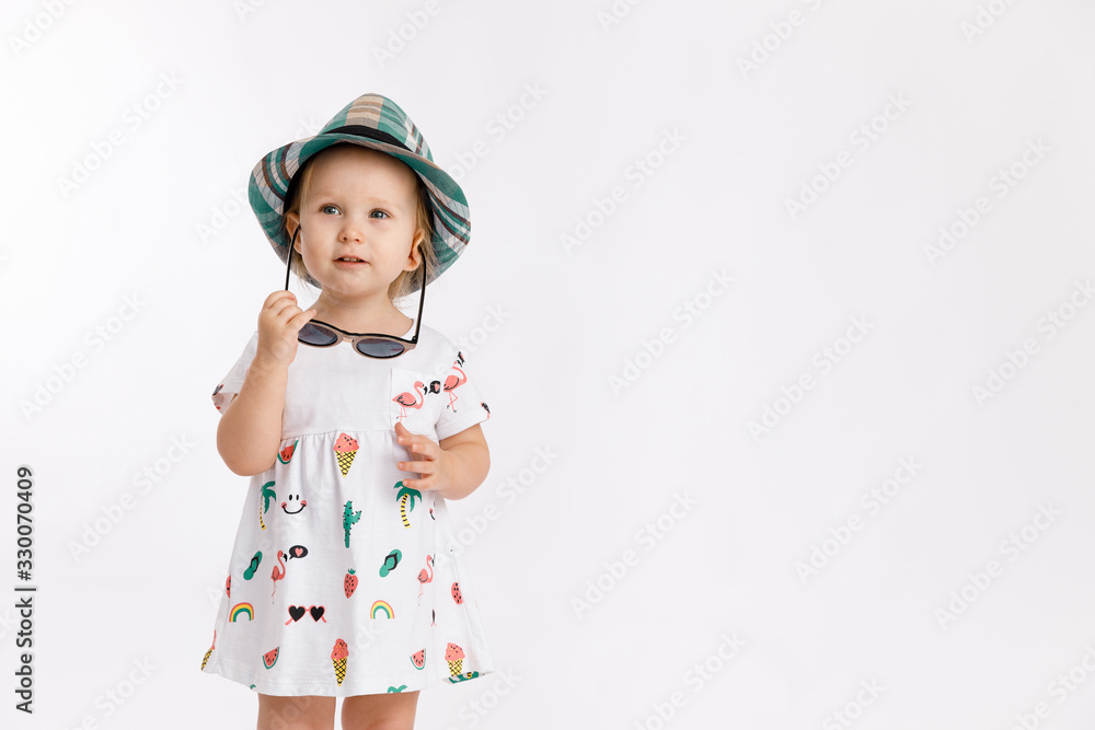 Portrait of a little cute girl wearing summer dress, blue checkered hat and fashion sunglasses isolated on white background. Concept of travel and summertime. Portrait of a little cute girl wearing summer dress, blue checkered hat and fashion sunglasses isolated on white background. Concept of travel and summertime.