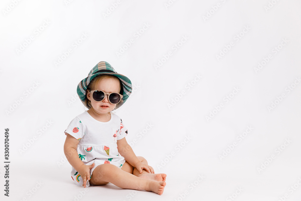 Portrait of a little cute girl wearing summer dress, blue checkered hat and fashion sunglasses isolated on white background. Concept of travel and summertime. Portrait of a little cute girl wearing summer dress, blue checkered hat and fashion sunglasses isolated on white background. Concept of travel and summertime.