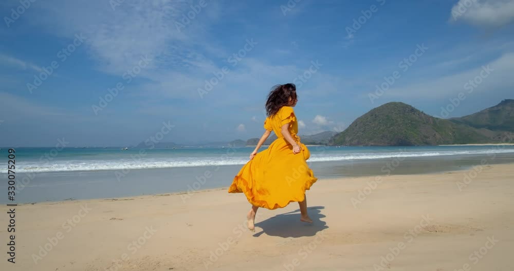 young happy brunette in yellow dress running along sand beach taking fresh air and admiring breathtaking seascape young happy brunette in yellow dress running along sand beach taking fresh air and admiring breathtaking seascape