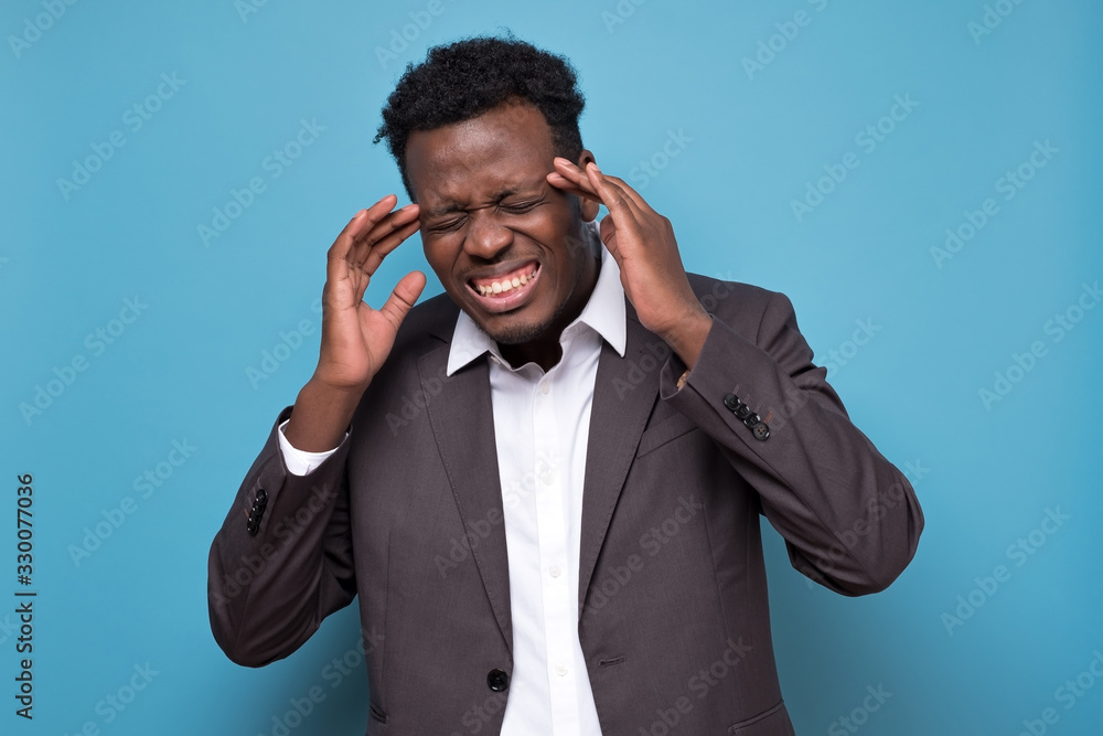 Serious afro american young man with strict headache in studio on blue isolated background Serious afro american young man with strict headache in studio on blue isolated background