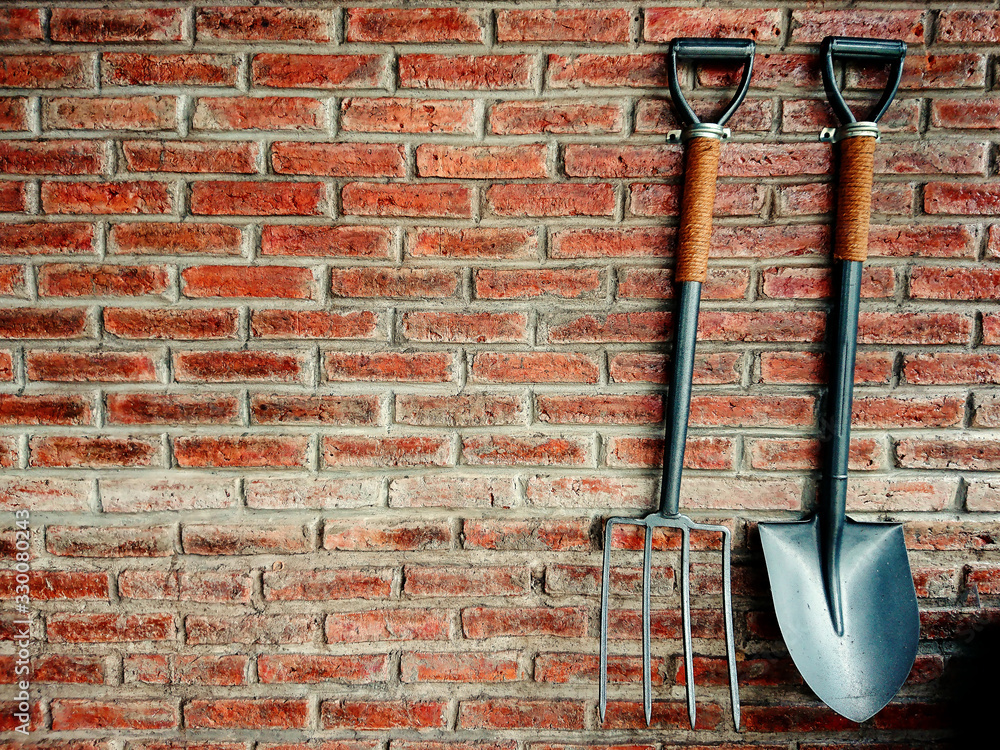 Shovel and rake on red brick wall. Gardening tools background Shovel and rake on red brick wall. Gardening tools background