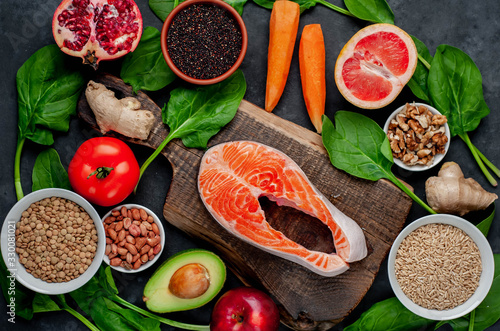 Selection of healthy food: salmon, fruits, seeds, cereals, superfoods, vegetables, leafy vegetables on a stone background. Healthy food for people.