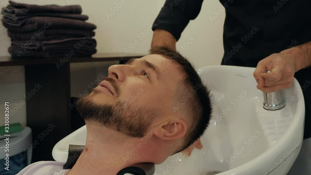 Cropped view of hairstylist preparing to wash head of client. Relaxed young man waiting while barber adjusting water temperature. Male beauty concept Cropped view of hairstylist preparing to wash head of client. Relaxed young man waiting while barber adjusting water temperature. Male beauty concept
