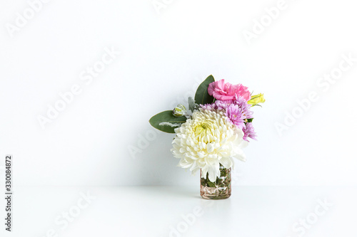 Beautiful floral arrangement of pink  purple and white flowers  in small glass vase on white table with a white background.