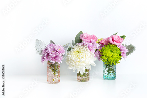 Wallpaper Mural Colourful pastel flowers of pinks, purples and greens, in glass vases on a white table with a white background.	 Torontodigital.ca