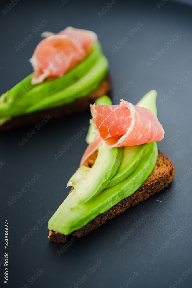 Avocado sandwich with jamon. Toasted bread for healthy breakfast or snack, copy space. Spanish tapas. Italian brushetta. Vegan avocado sandwich top view close-up
