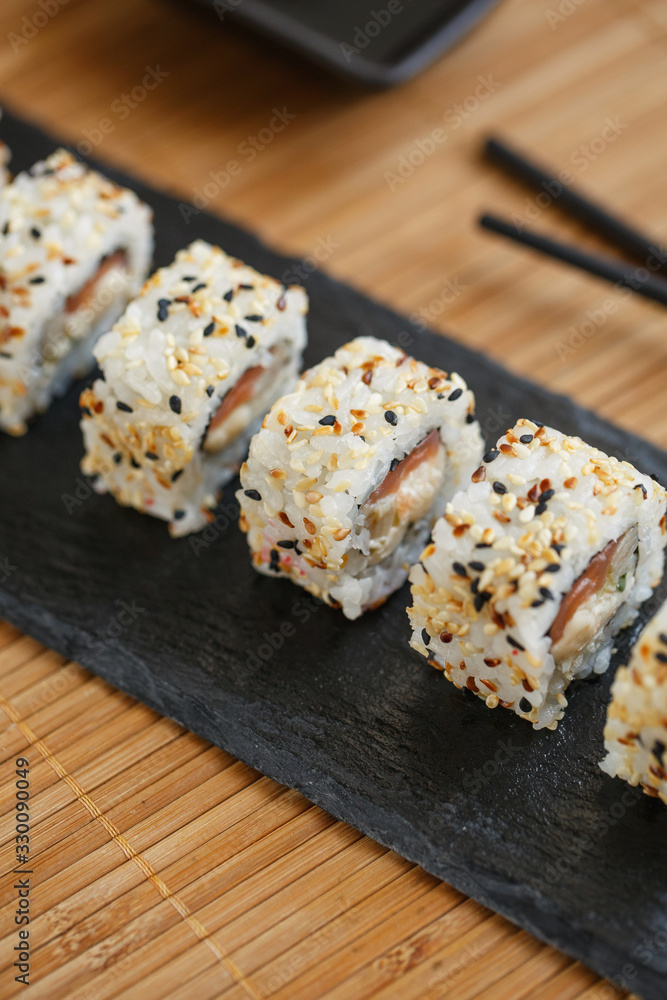 Japanese sushi rolls sprinkled with sesame seeds on a black stone board. Japanese sushi rolls sprinkled with sesame seeds on a black stone board.