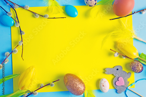 Happy Easter frame with yellow tulips, easter eggs, quail eggs, pussy-willow twigs with place for text in the middle. Easter background top view,copy space