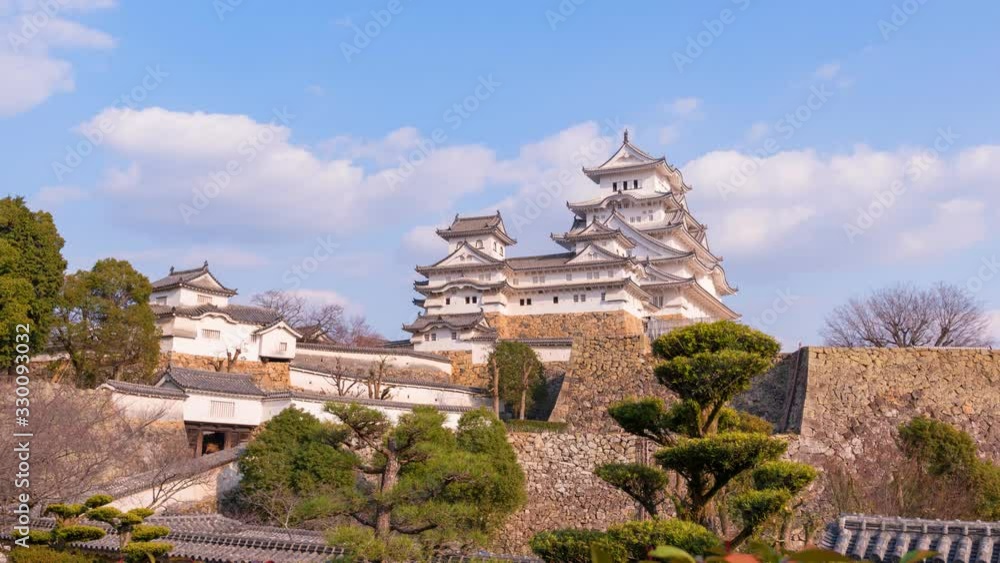 Timelapse Himeji old defence stone wall with architectural castle complex on hill with floating white clouds casting shadows Timelapse Himeji old defence stone wall with architectural castle complex on hill with floating white clouds casting shadows
