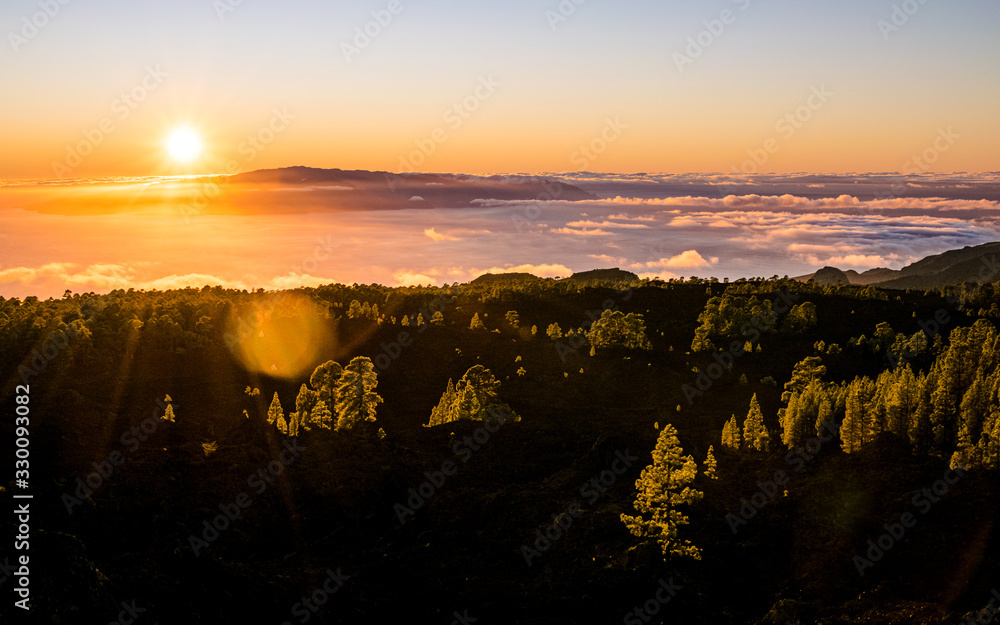 Gorgeous colorful sunset over the sea of clouds in Tenerife, with the La Gomera island on the horizon. Scenic landscape of Canary Islands, Spain. 