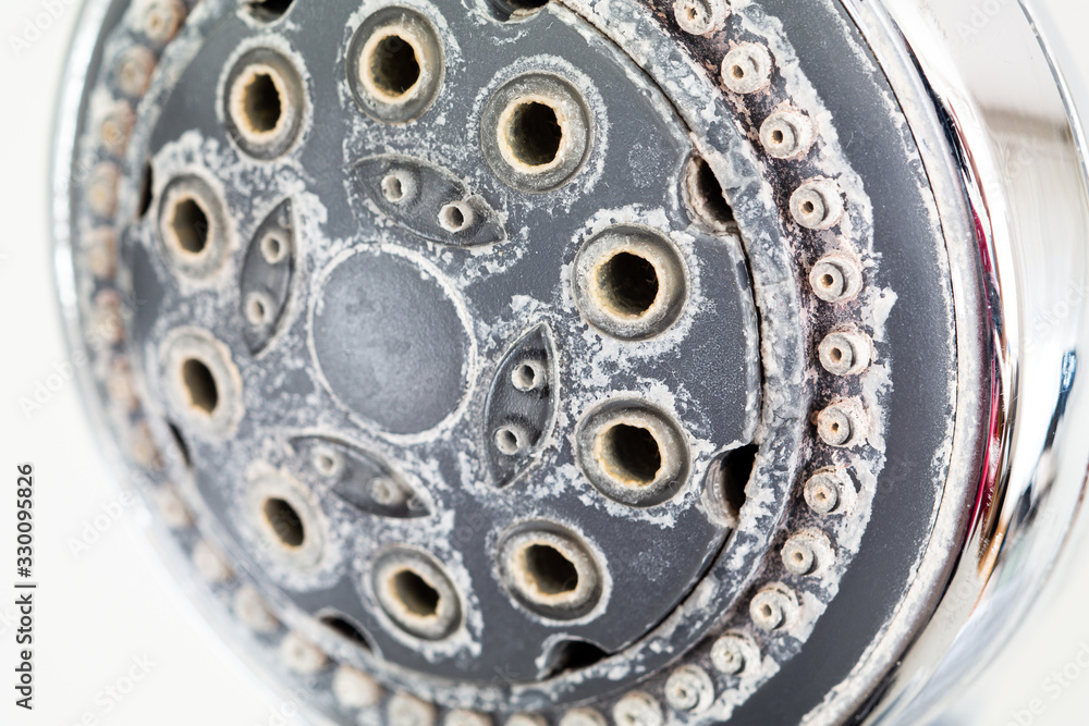 Silver round shower head with hard water deposits all around the sprinklers close up macro side shot isolated against light grey backdrop Silver round shower head with hard water deposits all around the sprinklers close up macro side shot isolated against light grey backdrop
