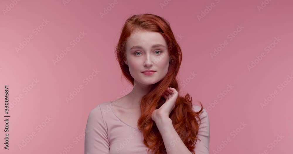 Beautiful red Haired Attractive woman standing in the Foreground at Studio. Posing on Camera and looking at Objective. Wearing Casual Clothes. Posing on Pink Background. Having Natural Beauty. Beautiful red Haired Attractive woman standing in the Foreground at Studio. Posing on Camera and looking at Objective. Wearing Casual Clothes. Posing on Pink Background. Having Natural Beauty.