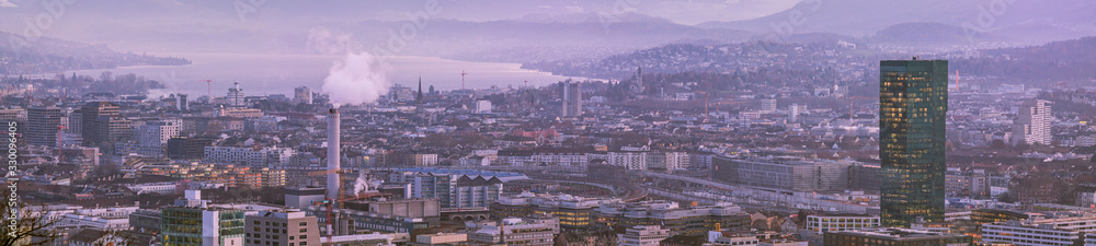 Beautiful panoramic vista view at dusk of Zurich city Switzerland from high vantage point in late autumn after sunset blue hour magenta tones lake visible in the distance