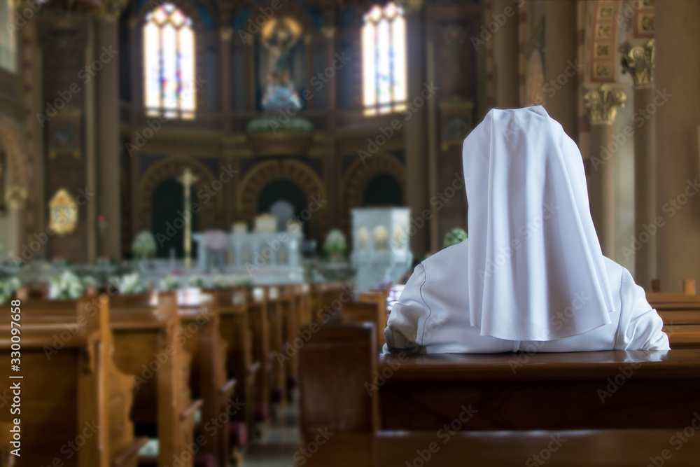 The one nun sits in the church and prays to God. A nun in traditional white robes meditates in a Christian cathedral. Prayer to Jesus.