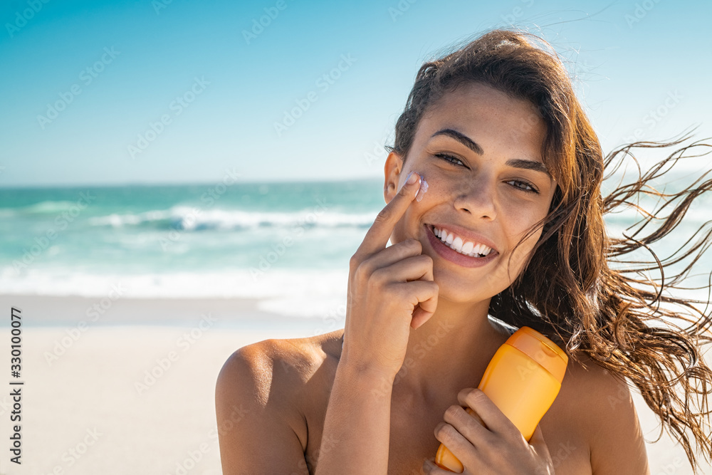 Smiling woman applying sunscreen - obrazy, fototapety, plakaty 