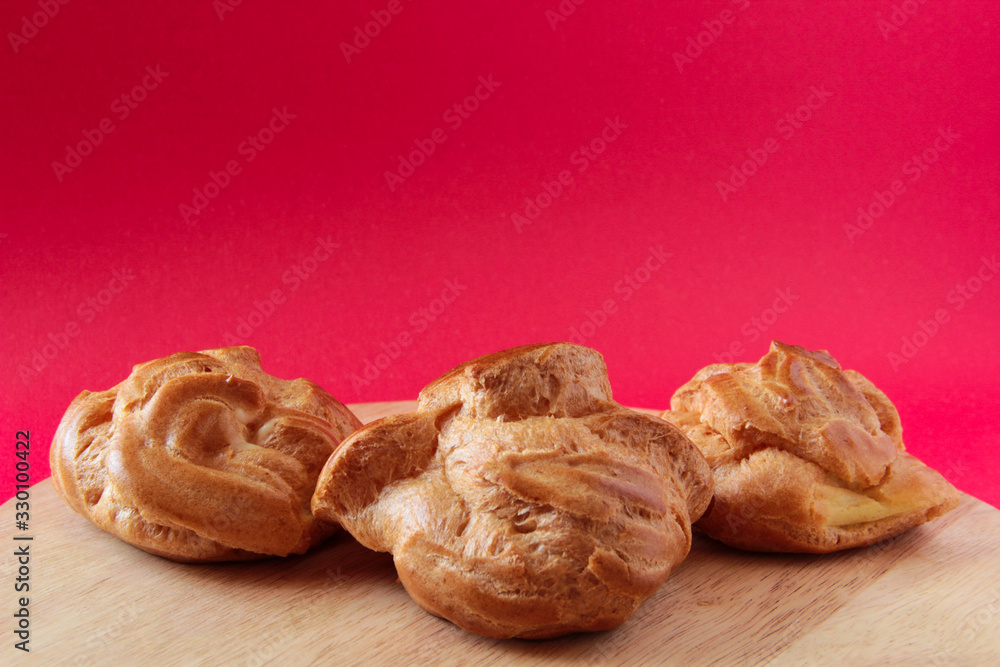Homemade profiteroles with custard, eclairs. On a wooden board, with a red background. French dessert.
