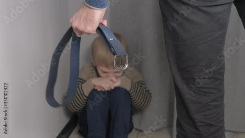 child abuse concept. father beats little son with domestic violence belt. upset punishment boy sits in lifestyle the corner hand swings to hit