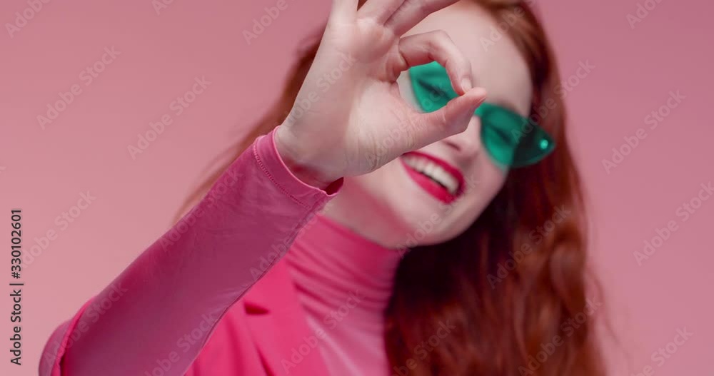 Portrait of Red haired Woman making Sign of goodness and Ok with her Fingers. Looking satisfied and Happy. Wearing trendy Pink Blazer and jacket. Having Modern Eyeglasses, demonstrating it. Portrait of Red haired Woman making Sign of goodness and Ok with her Fingers. Looking satisfied and Happy. Wearing trendy Pink Blazer and jacket. Having Modern Eyeglasses, demonstrating it.