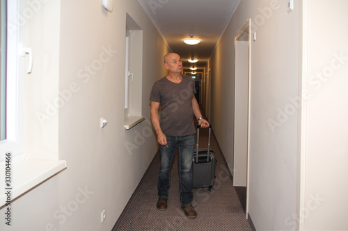 adult man walks down the hotel corridor to his room with a suitcase and keys in his hand, the concept of a long-awaited vacation, business trip