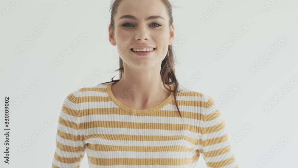 A pleased smiling young woman is correcting her hairstyle while looking to the camera isolated over white background in studio A pleased smiling young woman is correcting her hairstyle while looking to the camera isolated over white background in studio