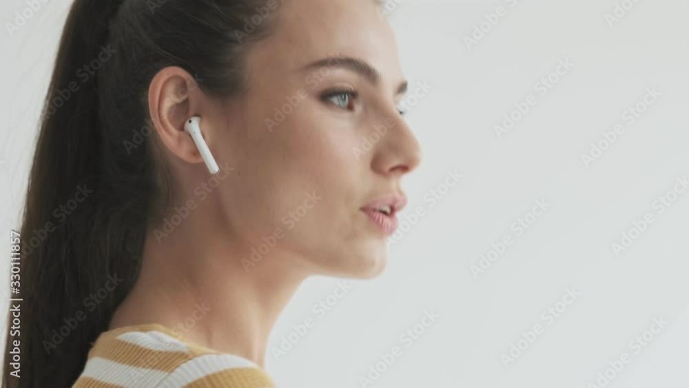 A side view of a happy young woman is using her wireless earphones isolated over white background in studio A side view of a happy young woman is using her wireless earphones isolated over white background in studio