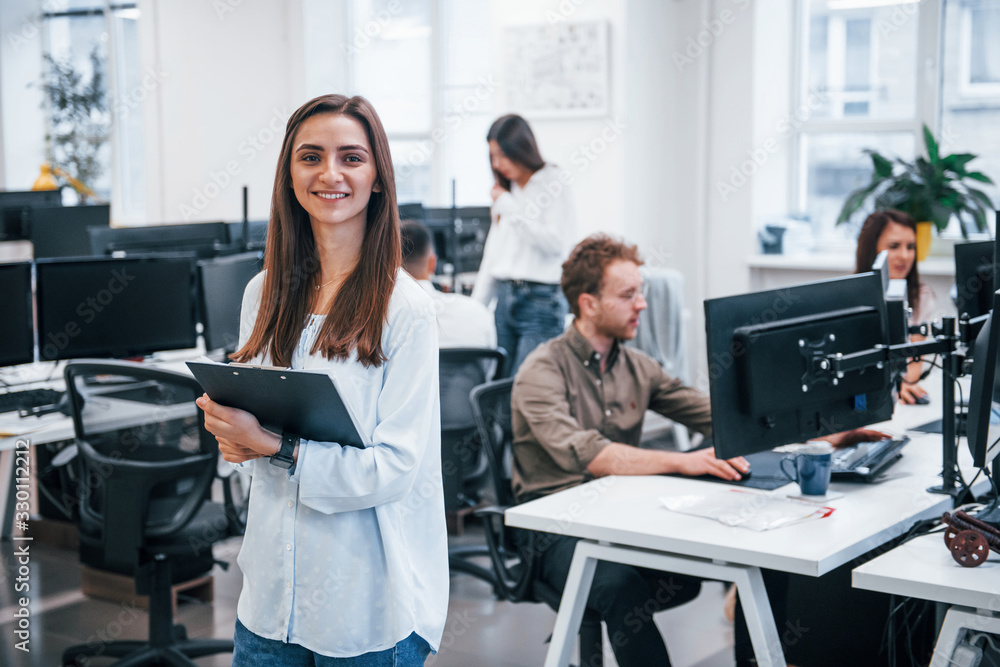 Woman with documents in hands standing in front of her colleagues in the office Woman with documents in hands standing in front of her colleagues in the office