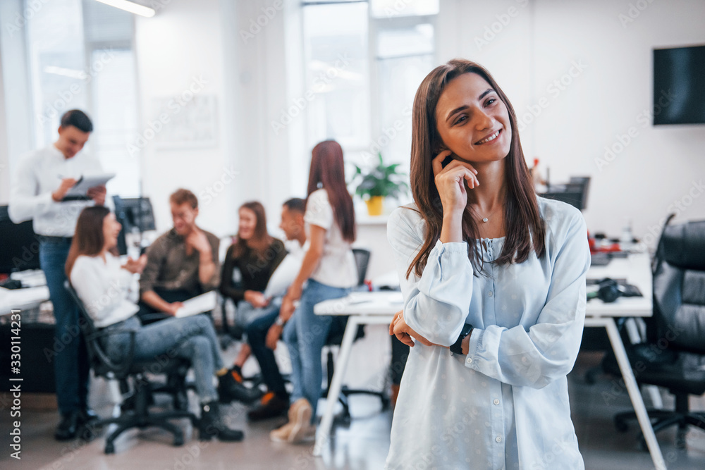 Positive woman standing in front of young business people that working together in the modern office Positive woman standing in front of young business people that working together in the modern office