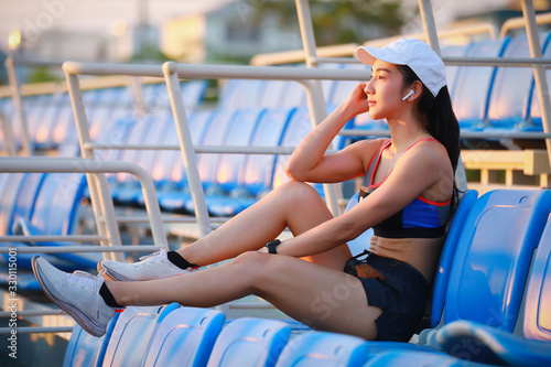 Asian woman relaxing with music after workout in the stadium seat