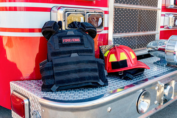 Ballistic vest and red firefighter helment on fire truck bumper. Concept of evolving role of fire department response to mass casualty shooting and terrorism