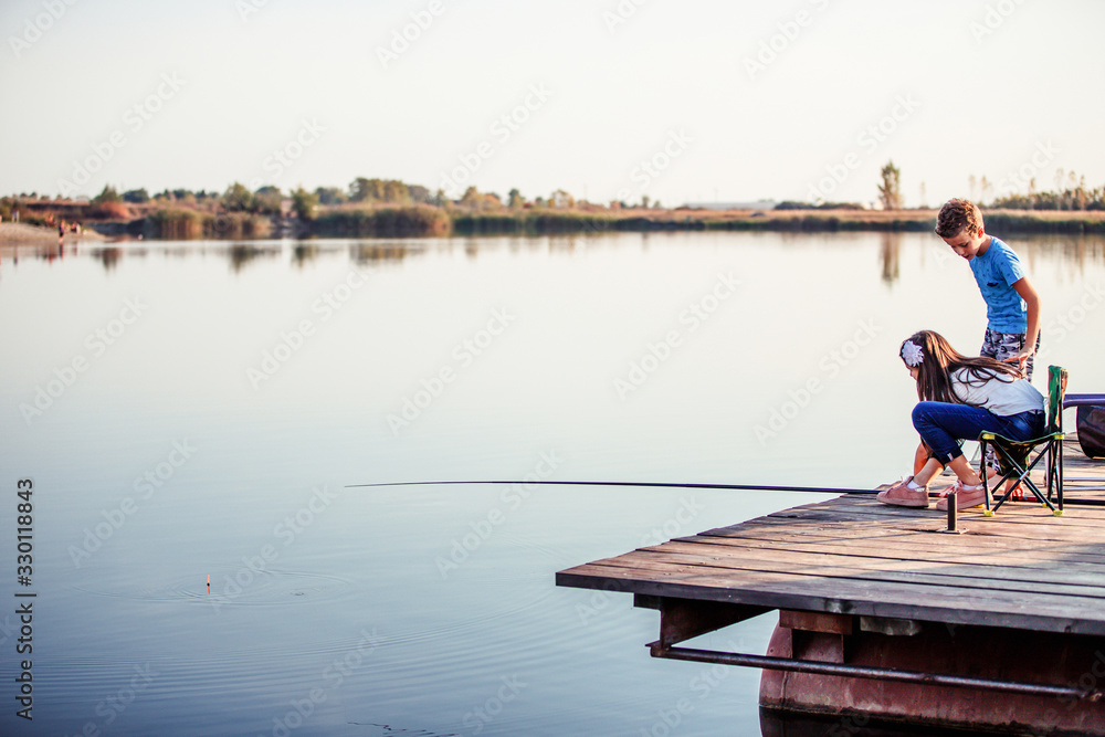 Naklejka premium Two cute little friends, boy and girl fishing on a lake in a sunny summer day