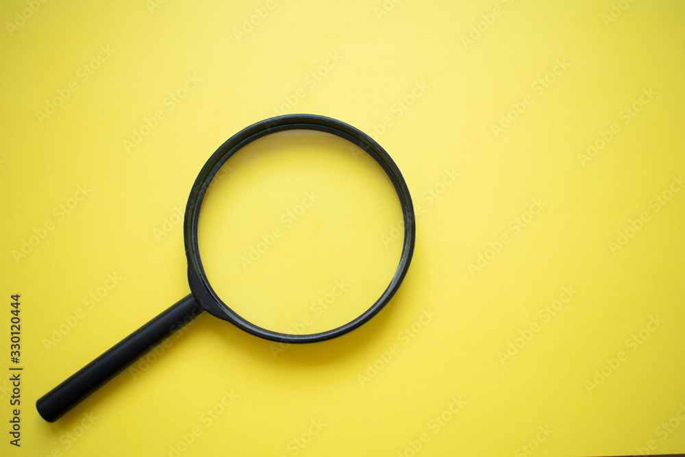 Magnifying glass isolated on bright yellow background, bottom left corner Magnifying glass isolated on bright yellow background, bottom left corner