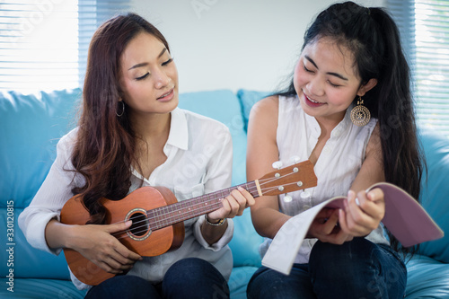 Two asia women are having fun playing ukulele and smiling at home for relax time