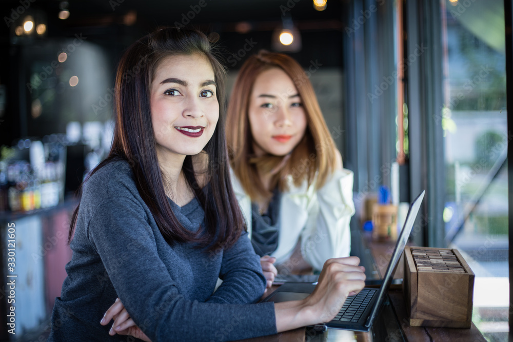 Two Asian business women using notebook working and Discussion of the important contract at coffee shop Two Asian business women using notebook working and Discussion of the important contract at coffee shop