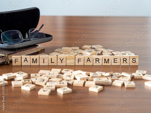 family farmers concept represented by wooden letter tiles on a wooden table with glasses and a book photo