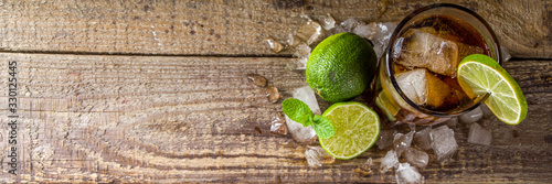 Summer iced alcohol drink with cola and lime. Rum and cola Cuba Libre cocktail. One long glass on wooden background copy space