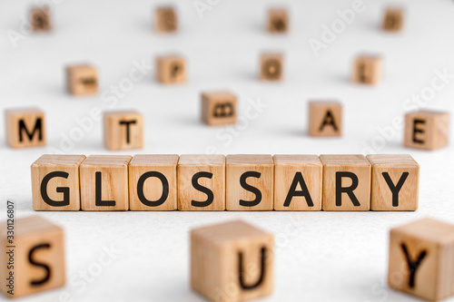 Glossary - word from wooden blocks with letters, alphabetical list of terms glossary concept, random letters around white background