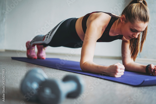 Attractive fit young woman in sport wear girl trains with dumbbells make plank at loft studio