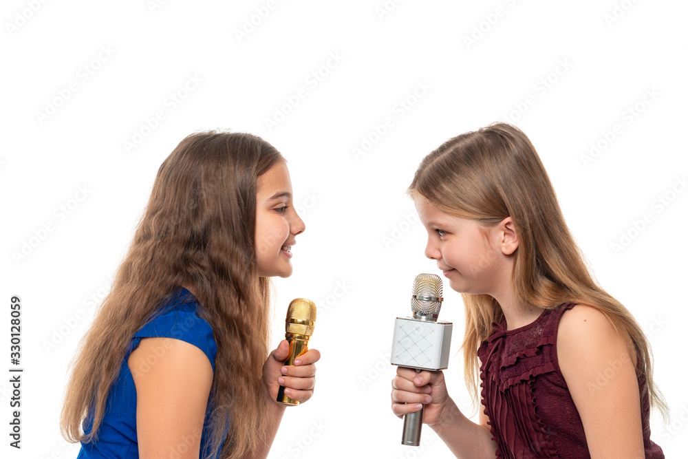 Two attractive girls brunette and blonde sing songs while holding microphones in their hands, isolated Two attractive girls brunette and blonde sing songs while holding microphones in their hands, isolated