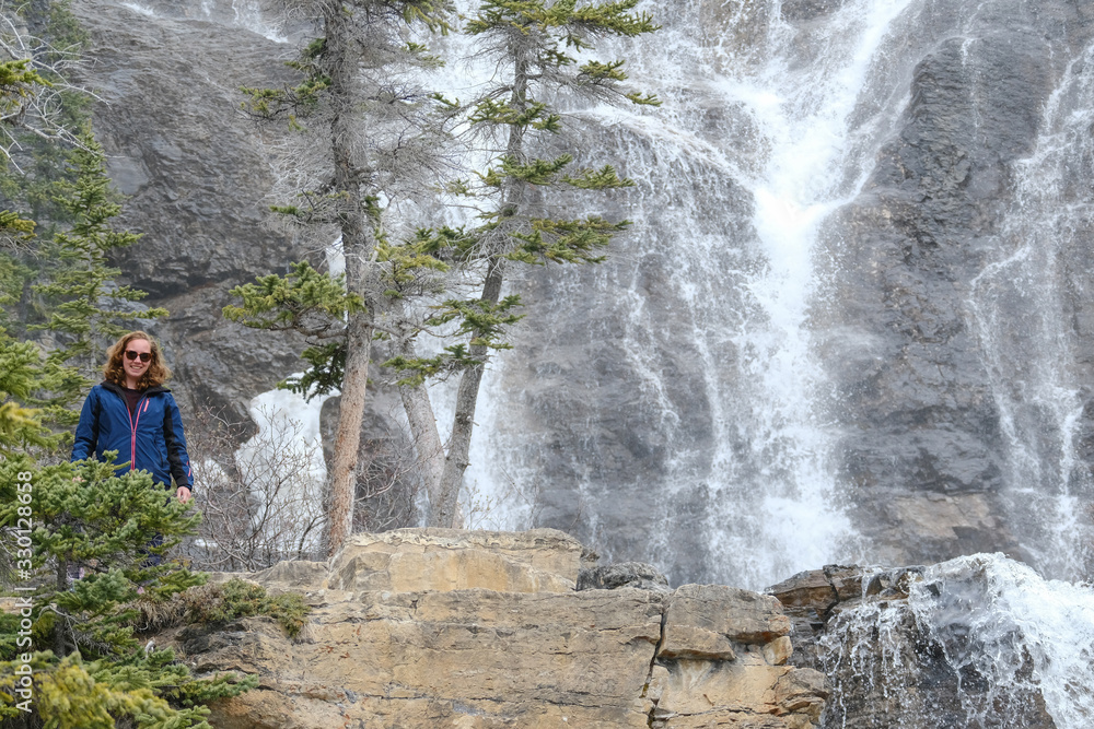 Woman standing en smiling in casual clothing. Cascading Tangle Creek Falls in Jasper National Park, Alberta, Canada Woman standing en smiling in casual clothing. Cascading Tangle Creek Falls in Jasper National Park, Alberta, Canada