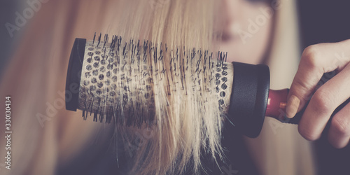 Round brushing combs long blond hair closeup.