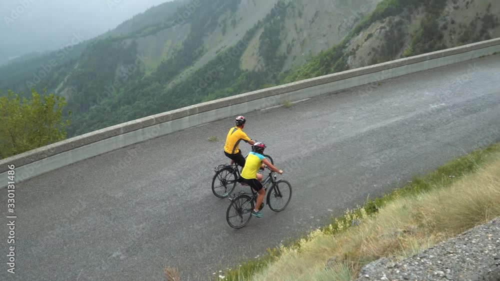 Two friends bikers ride bicycles in mountains, road biking, picturesque scenery. Sportsmen drive the route of Tour de France competition in french Alps Two friends bikers ride bicycles in mountains, road biking, picturesque scenery. Sportsmen drive the route of Tour de France competition in french Alps